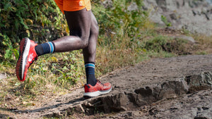 A trail runner midstride running up a trail wearing the best socks for running by darn tough